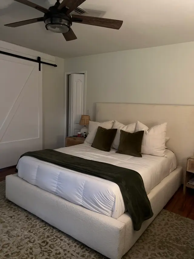 Made white bed with dark green pillows beside a sliding barn door