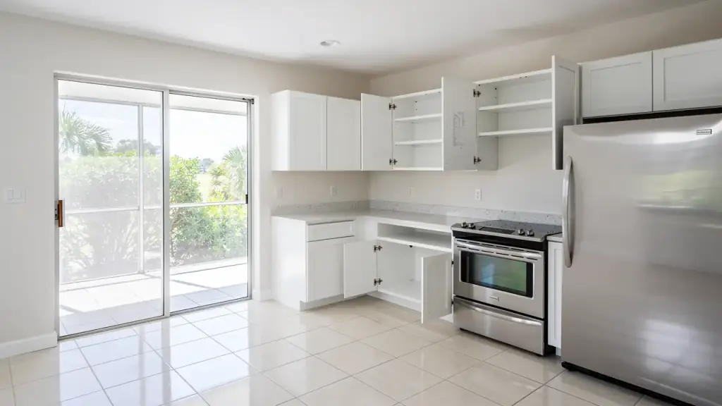 Empty white kitchen with cabinet doors open on wiped shelves and stainless appliances